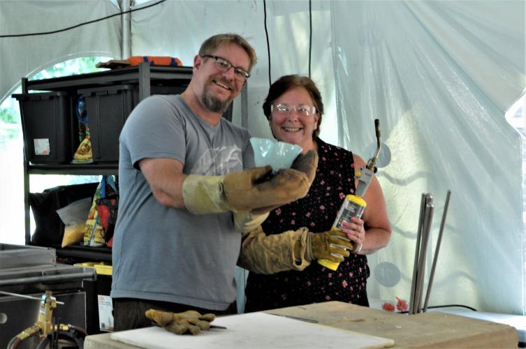Connie holding a blow torch and showing off her bowl standing next to Greg