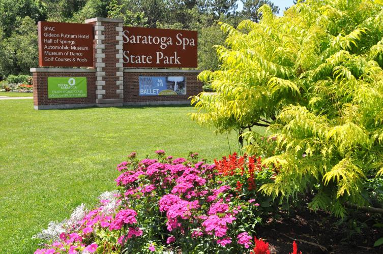 Saratiga Spa State Park sign at entrance with colorful bush and flowers in the foreground