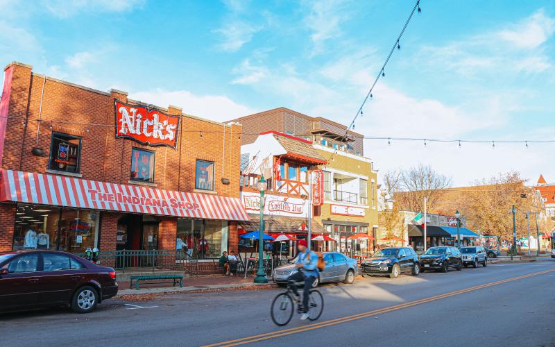 A person riding a bike past Nick's and The Indiana Shop on Kirkwood Avenue during an early winter day