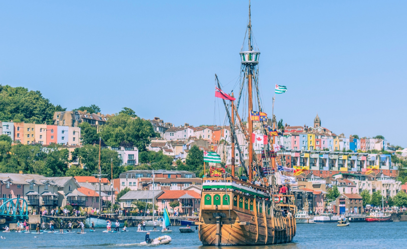 The Matthew ship sailing eastwards along Bristol Harbourside with paddleboarders and the colourful houses of Cliftonwood in the background during the Bristol Harbour Festival - credit Jim Cossey