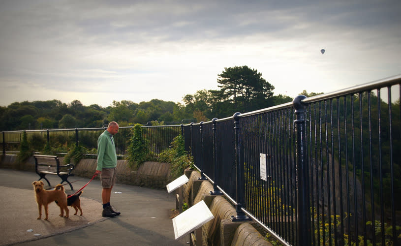 A man in a green jumper and orange hat walking two dogs on The Downs Bristol CREDIT Ann Brook