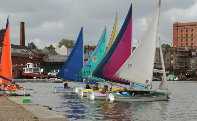 A row of boats with colourful sails on the water in Bristol Harbour - Credit All Aboard Watersports