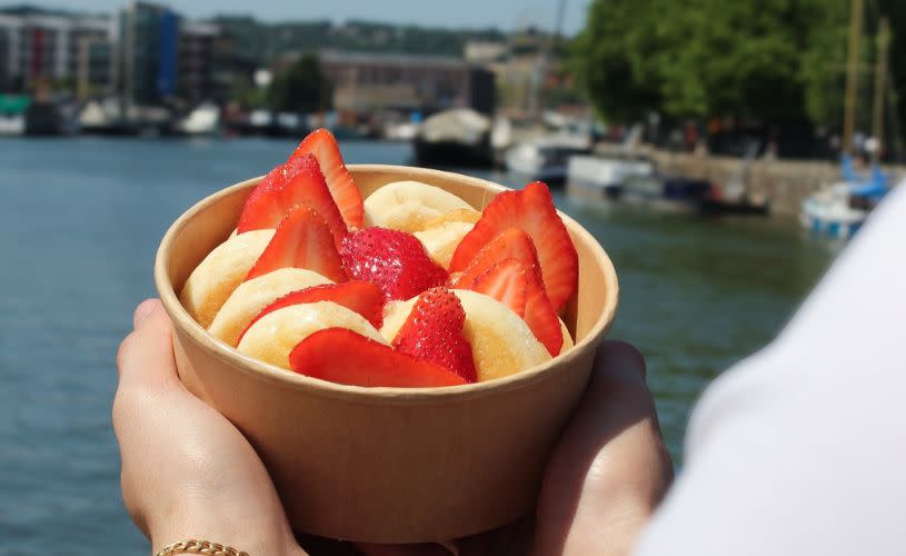 Hands holding a container of mini pancakes and strawberries - credit The Pancake Man
