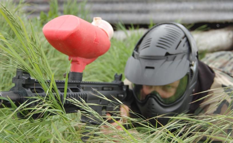 A person lying in tall grass aiming a paintball gun at Bristol Activity Centre - credit Bristol Activity Centre