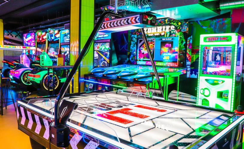 Brightly lit bar interior with arcade machines and air hockey table - credit King Pins