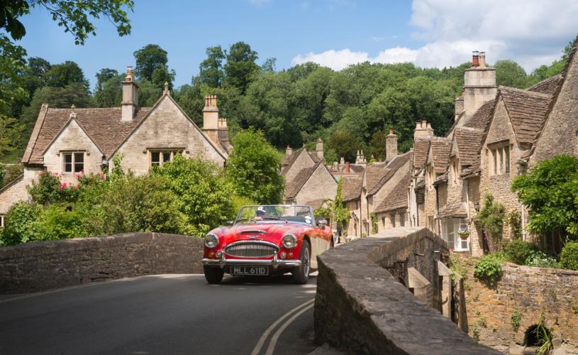 A red vintage sports car driving over the bridge in the village of Castle Combe, near Bristol - credit Great West Way