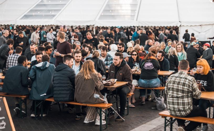 People sat on wooden benches outside drinking beer - Credit Craft Beer Festival