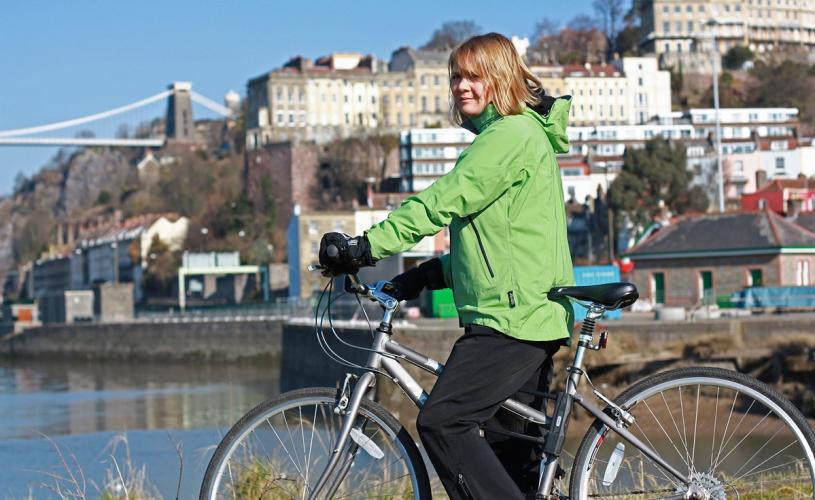 A women wearing a green jacket on a bike with Clifton Suspension Bridge in the background - Credit Chris Bahn