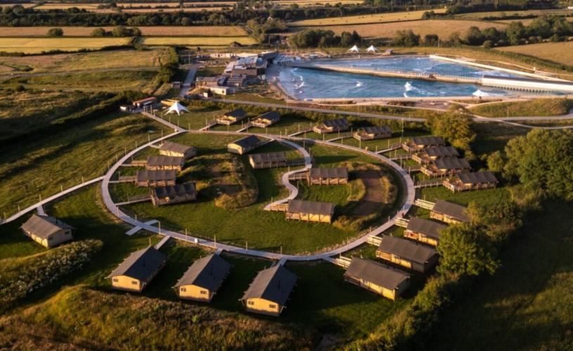 An aerial drone shot of The Wave and Camp at The Wave showing lodges and the Wave surfing lake in the background
