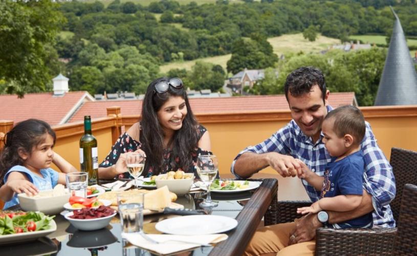 A family of 4 eating lunch at a table with a view of the Mendip Hills - Credit Wookey Hole