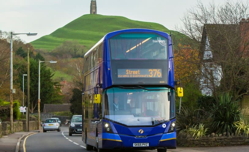 A blue double decker bus with Glastonbury Tor in the background