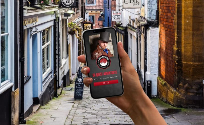 Go Quest Adventures promo image of the website or app on the phone with a Bath street background.