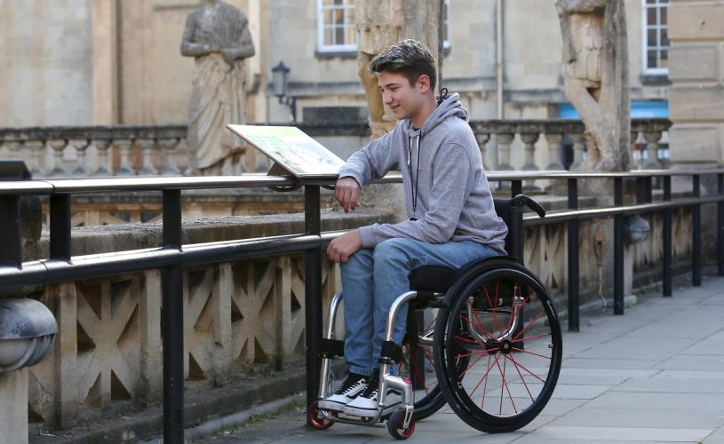 A man in a wheelchair reading a sign at The Roman Baths