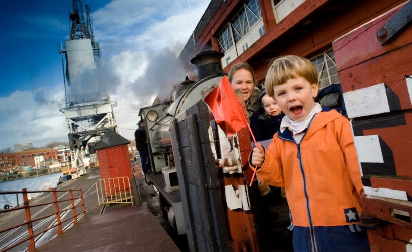 A small child wearing an orange coat on a steam train outside M Shed