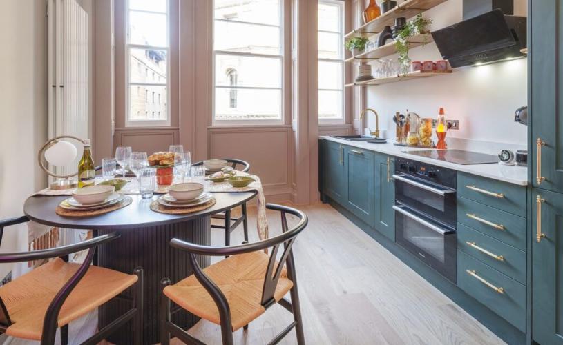 A dark green galley kitchen with a brown wooden table- credit Mint Stays