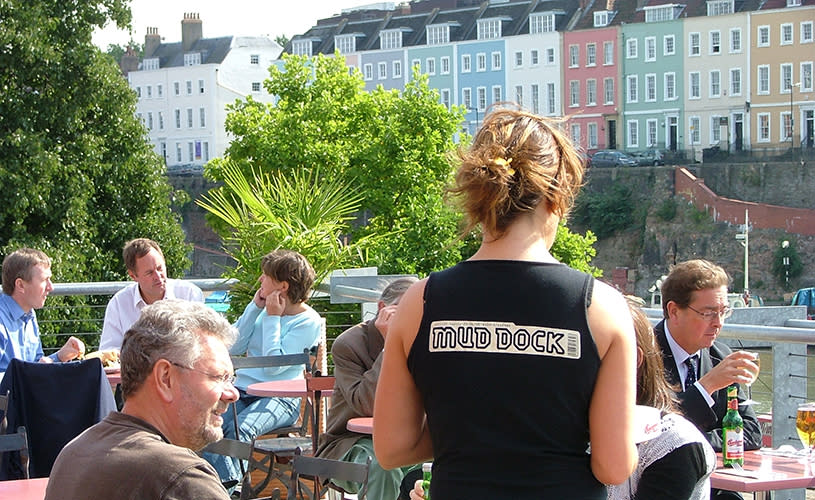 A women wearing a black tank top serving people on a terrace - Credit Mud Dock