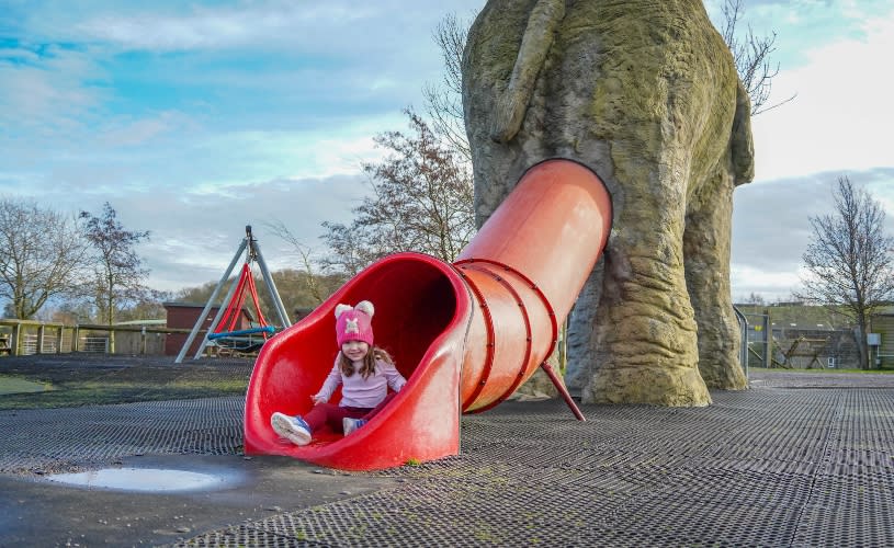 A small child wearing a pink hat sat at the bottom of a red slide