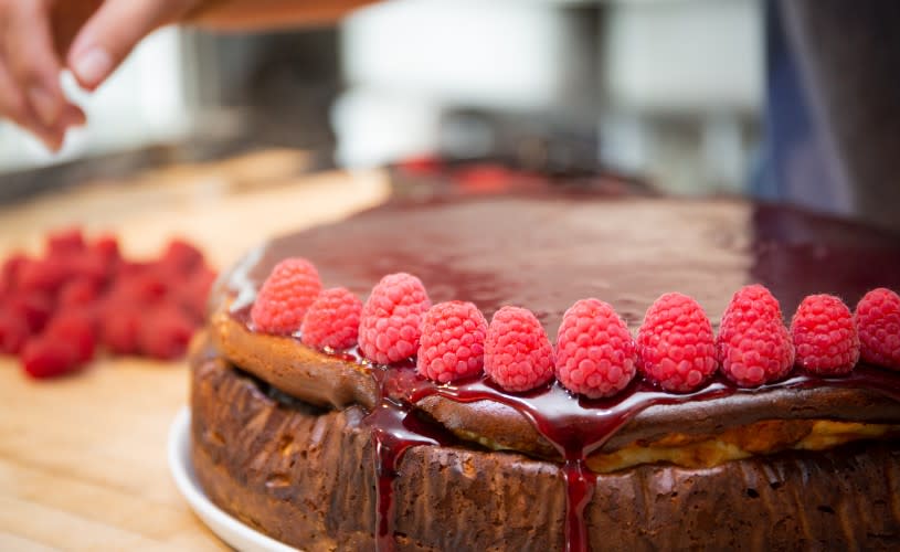 A cake topped with a red sauce and raspberries - Credit Papadeli