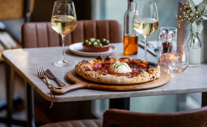 A pizza on a table with two glasses of wine at Pizza on the Park in central Bristol - credit Evoke Pictures