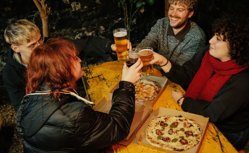 Pizzarova - Four friends saying cheers over takeaway pizza