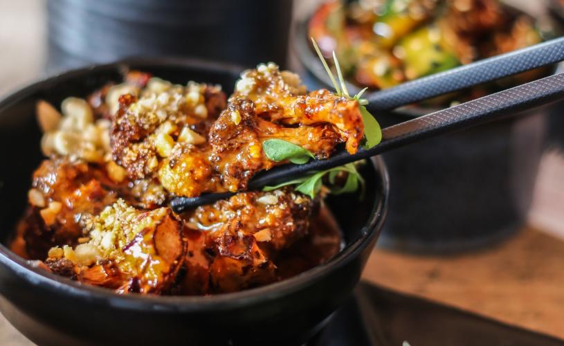 Fried cauliflower in sauce being picked up with chopsticks - credit Seven Lucky Gods
