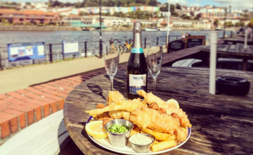 A plate of fish and chips with a bottle of wine and 2 glasses at The Cottage Inn - Credit The Cottage Inn