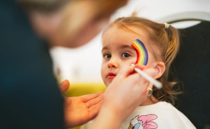 A little girl having a rainbow painted on her face