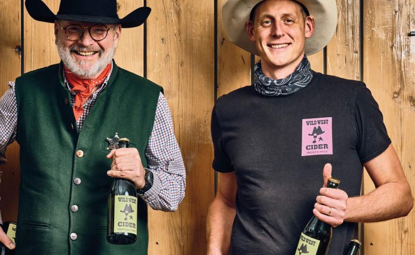 Two men dressed in cowboy hats holding bottles of cider - credit Wild West Cider