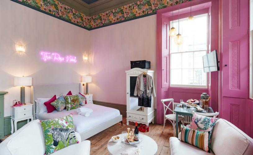 A lounge area with large window, pink wall and white furniture - credit Mint Stays