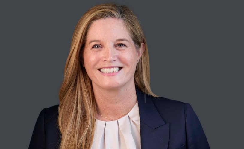 A women in front of a grey background wearing a white shirt and a navy blue blazer
