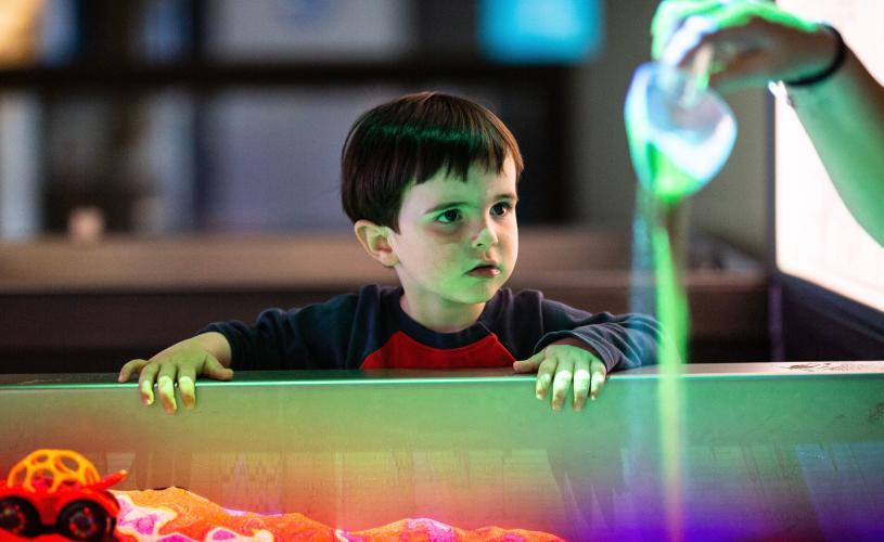 A child watching someone pour sand in a play area at the We The Curious science centre in Bristol - credit Lisa Whiting