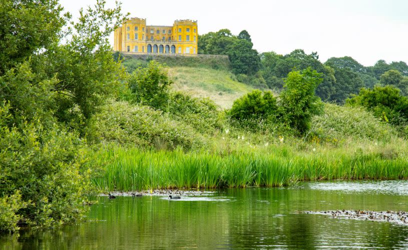 The yellow Dower House on a hill overlooking some trees and a fishing pond.