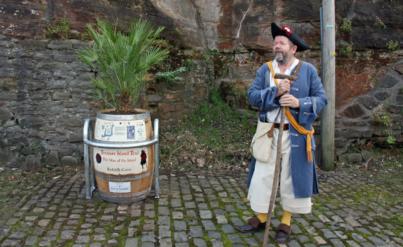 A man wearing a pirate outfit stood next to a wooden barrel - Credit Visit West