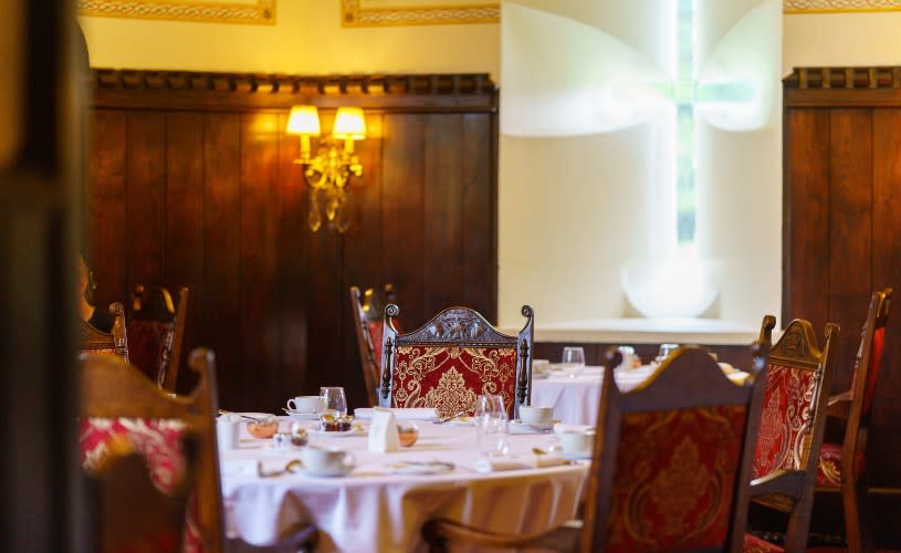 A darkened restaurant with red fabric chairs and wooden panelled walls - Credit Thornbury Castle