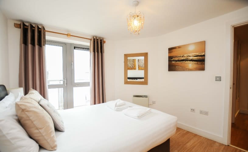 A bedroom with a large white bed and a picture of a sunset - Credit Your Apartment