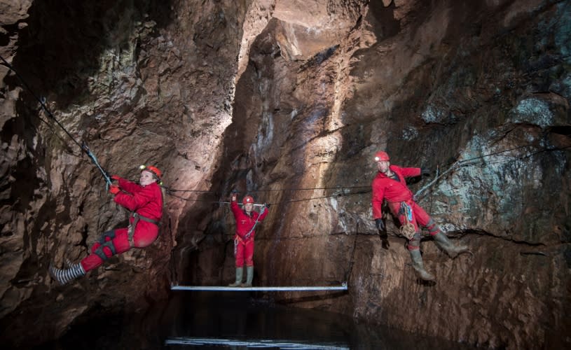 3 people wearing red all in one suits climbing on the side of caves at Wookey Hole