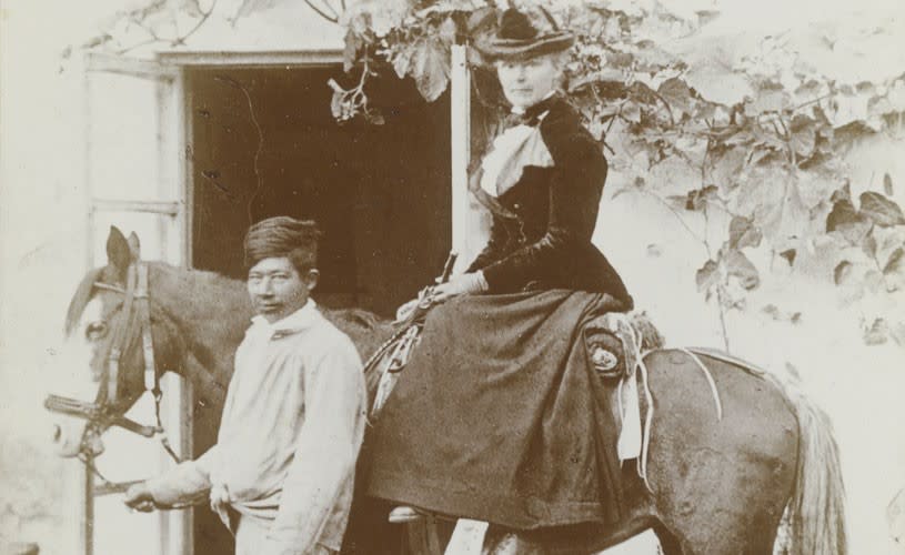 Black and white photo of a woman on a horse being led by a man