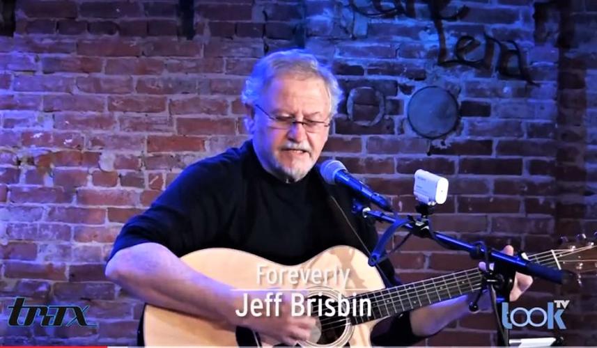 Jeff playing guitar in front of brick wall at Caffe Lena