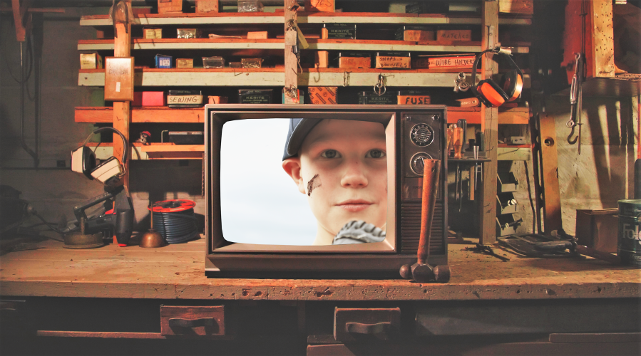 Television sitting on a cluttered work bench with the face of a young boy on the screen