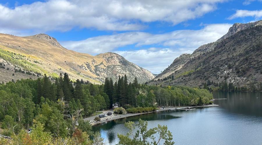 A view from a bit above a lake with mountains, clouds, and trees