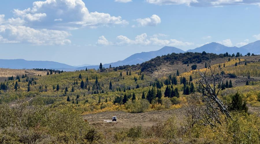 An RV driving on Monitor Pass with blue skies, clouds, and fall colors - green yellow and orange aspen - along with evergreens and browning grasses