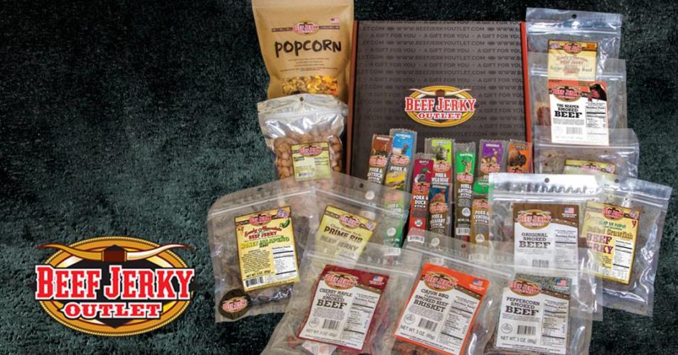 Display of bags of jerky, popcorn and other snacks on gray carpet with logo in lower left hand corner.