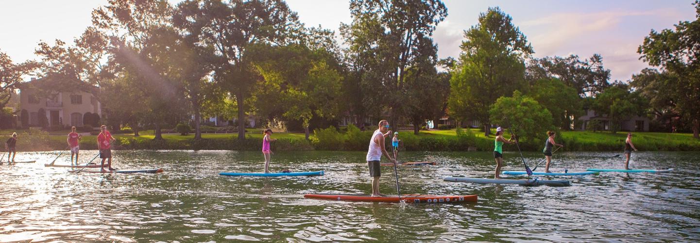People stand-up paddle-boarding down peaceful river
