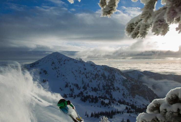Skier coming down steep slope with Wasatch Mountains and clouds behind them