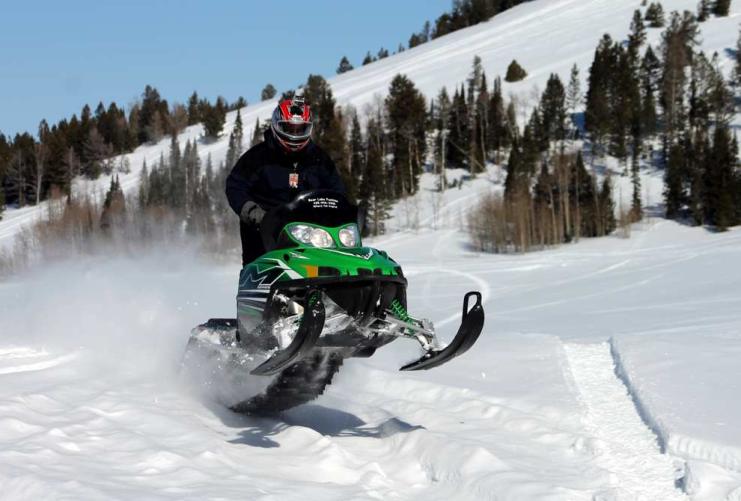 Green snowmobile jumping off snow