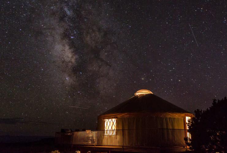 View of the Milkyway above a lit yurt in Moab