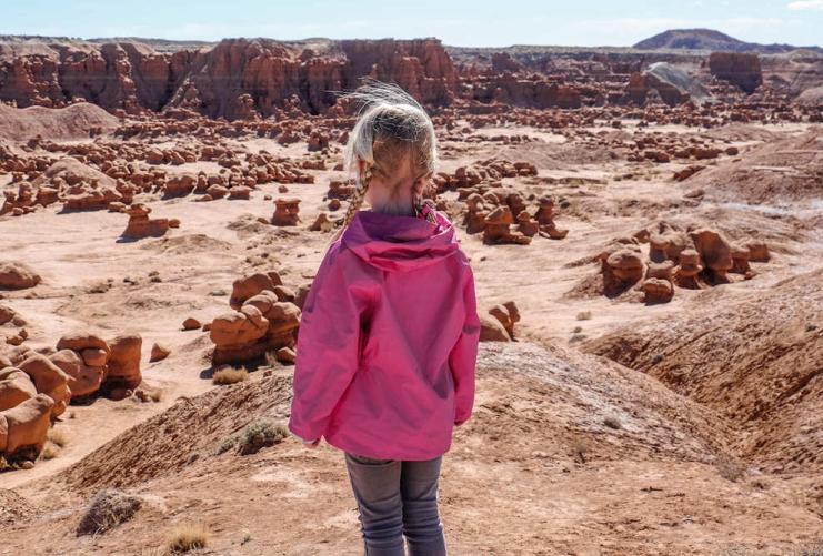 Girl in a pink jacket looking at the rocks and boulders of Goblin Valley State Park.
