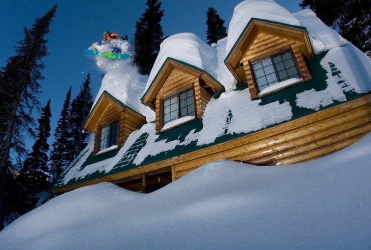 Snowboarder jumping off cabin roof in deep powder