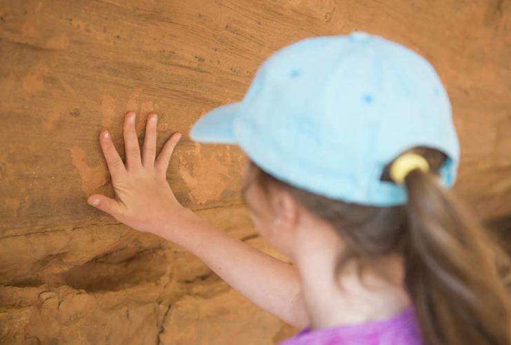 Young girl standing at hand print rock art