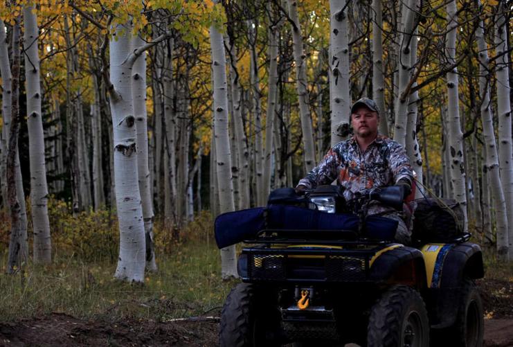 Outdoorsman on a four wheeler with aspen trees in the background.